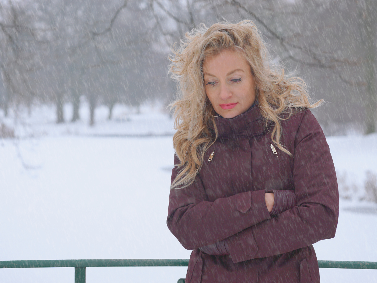lonely woman with blond hair in brown coat with snow in background