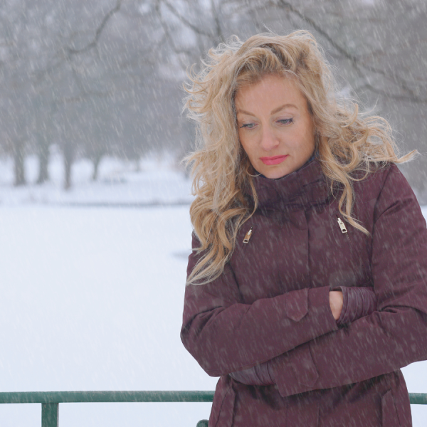 lonely woman with blond hair in brown coat with snow in background